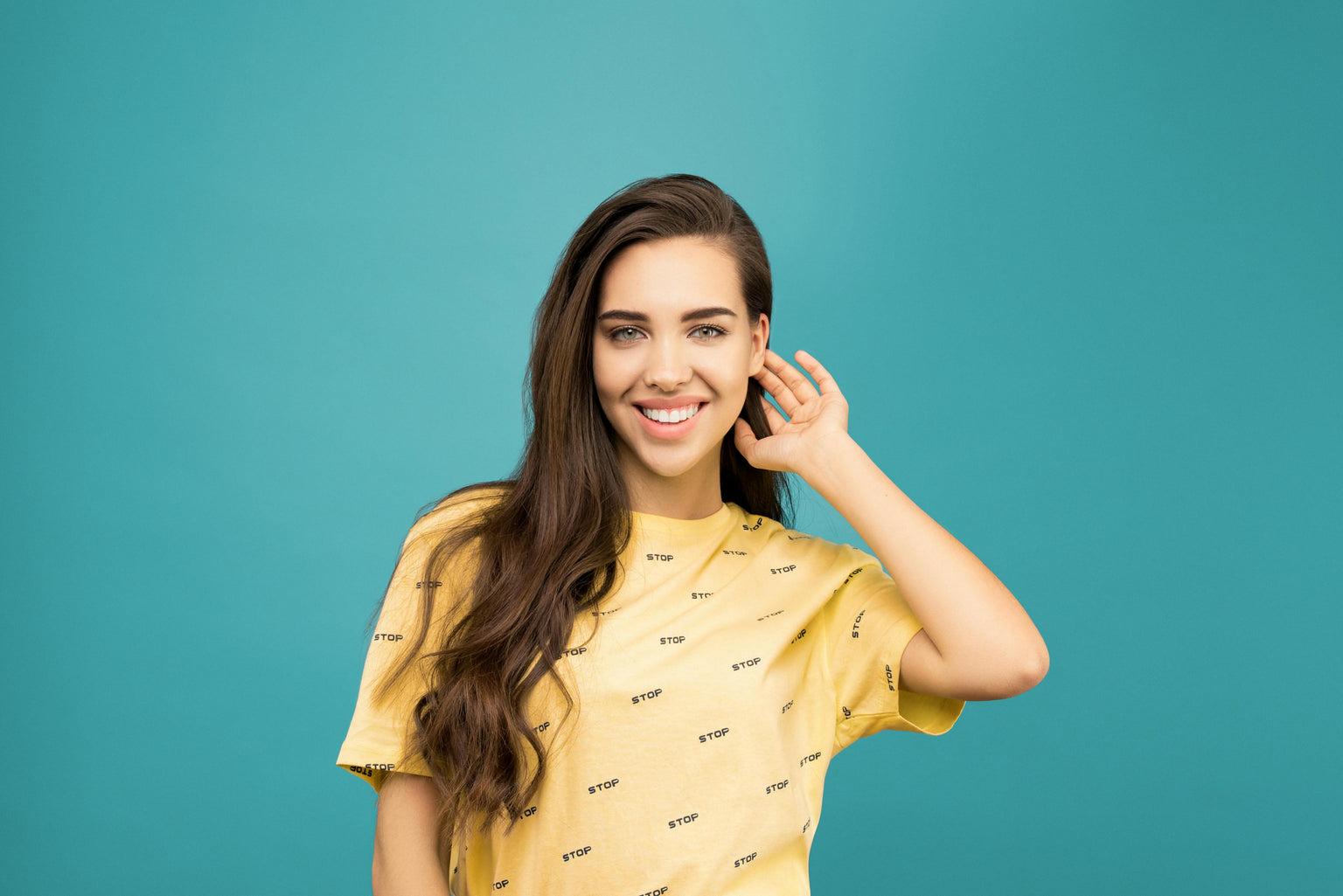 Woman in a yellow shirt with text on it, posing against a teal background